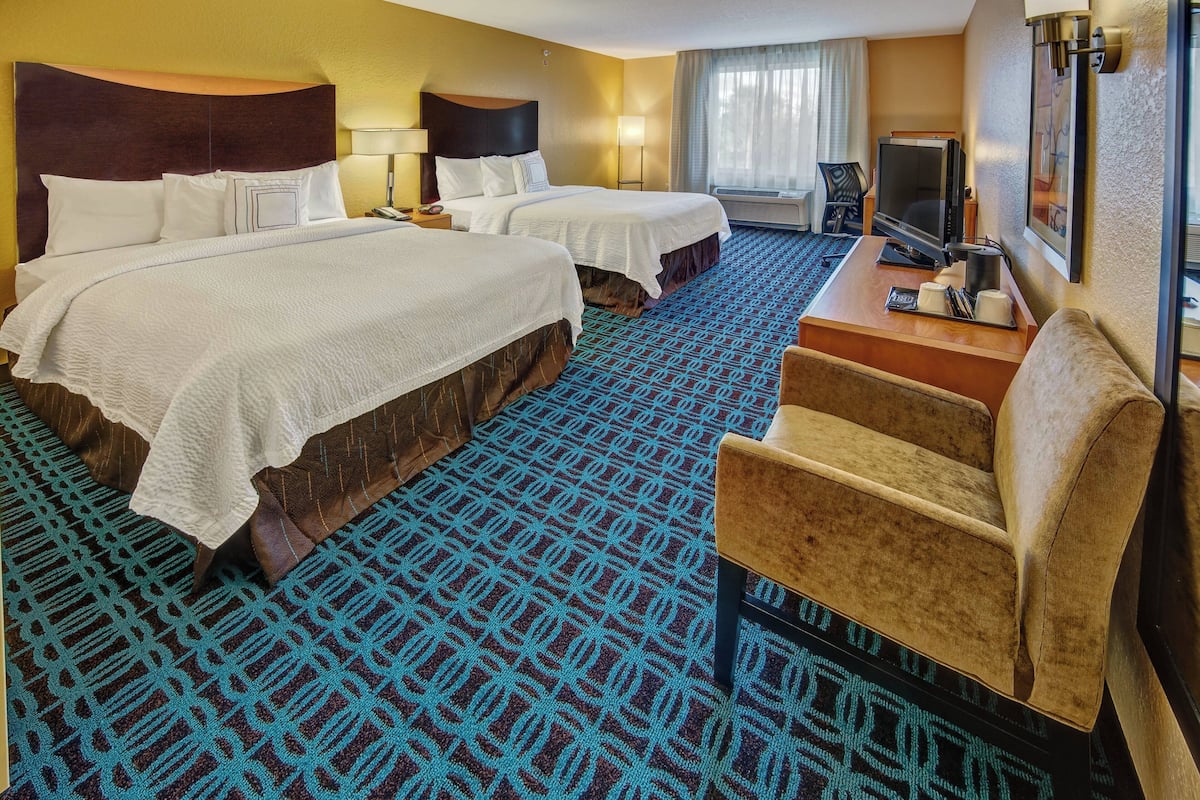Quarto de hotel com duas camas, uma escrivaninha e uma televisão, e um tapete estampado.