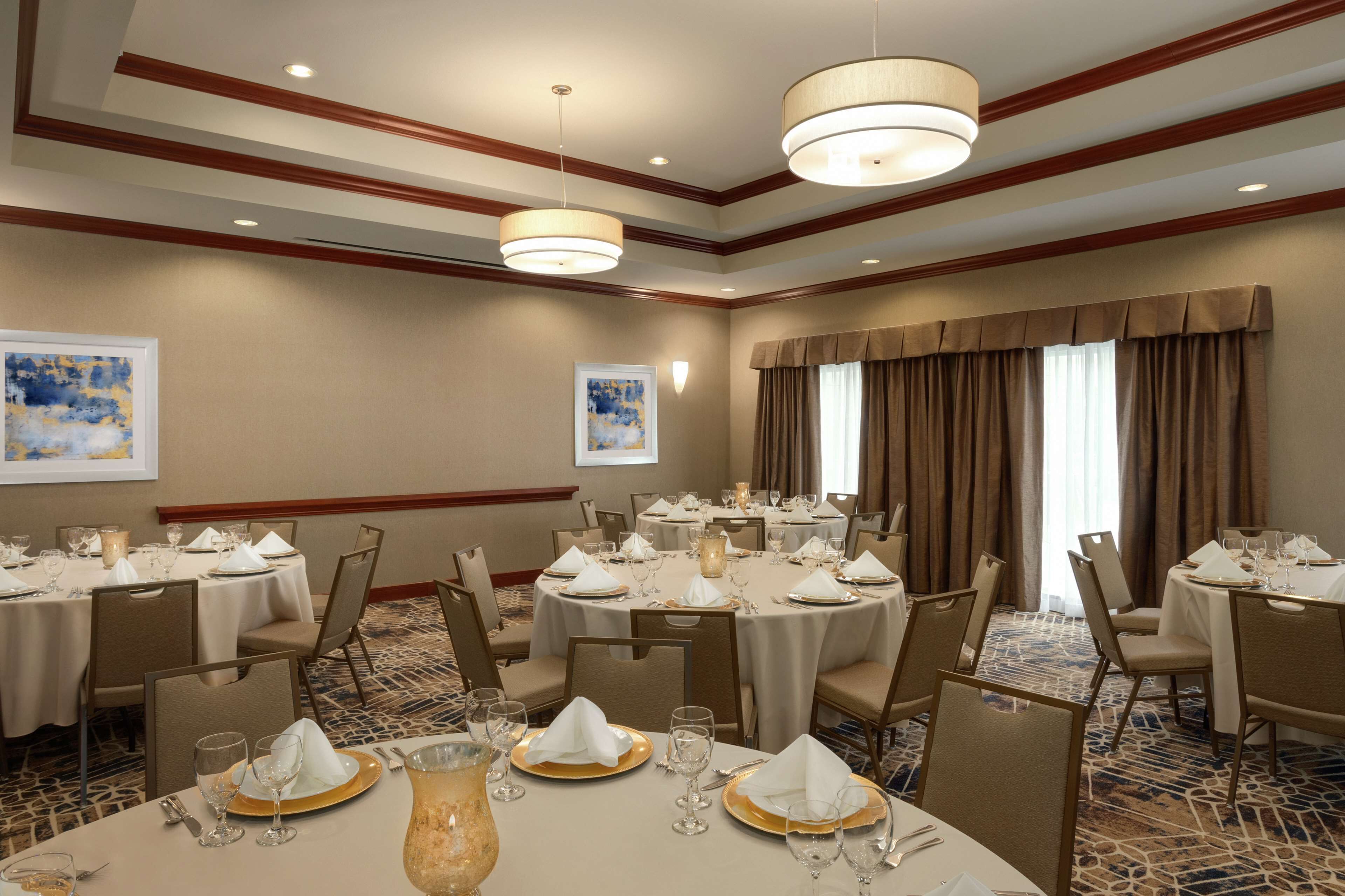A banquet hall with round tables set for dining, featuring white tablecloths, gold chargers, and glassware.