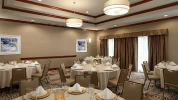 A banquet hall with round tables set for dining, featuring white tablecloths, gold chargers, and glassware.