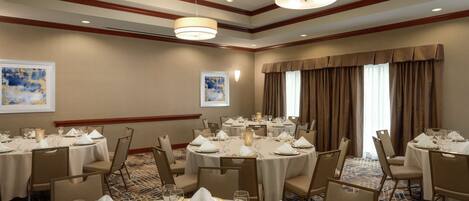 A banquet hall with round tables set for dining, featuring white tablecloths, gold chargers, and glassware.