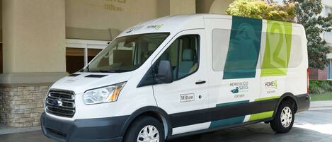 A white van with green and blue branding parked in front of a building with "HOMEWOOD SUITES" signage.