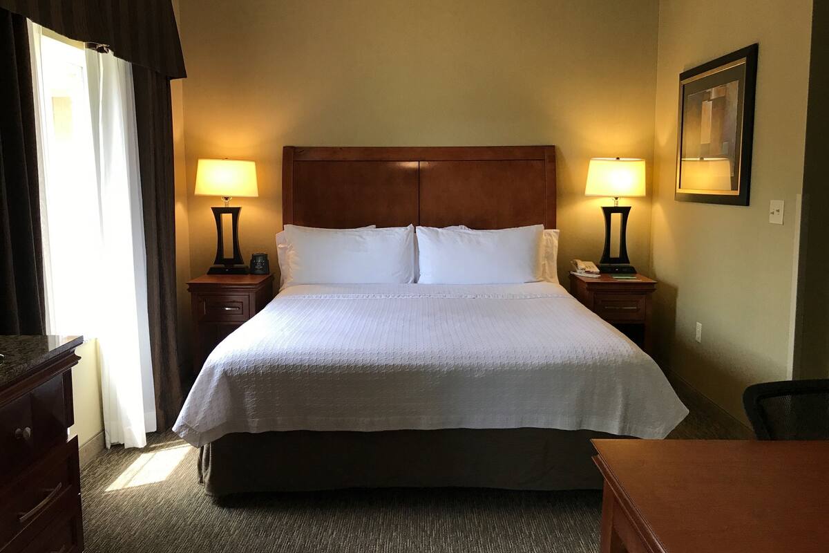 Ein Hotelzimmer mit einem großen Bett, zwei Nachttischen mit Lampen, einem Holz-Kopfteil und einem gerahmten Bild an der Wand.