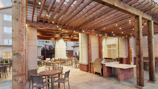 An outdoor patio area with wooden pergola, string lights, and a barbecue station. - Homewood Suites by Hilton Fort Smith (Fort Smith)