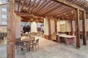 An outdoor patio area with wooden pergola, string lights, and a barbecue station. - Homewood Suites by Hilton Fort Smith (Fort Smith)