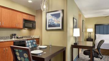 A hotel room with a kitchenette, dining area, and a bed.