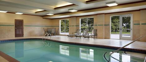 An indoor swimming pool with clear water, a pool ladder, and lounge chairs.