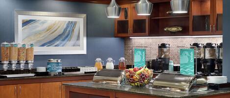A modern kitchen with wooden cabinets, a marble backsplash, and a breakfast bar with various food items and beverages.