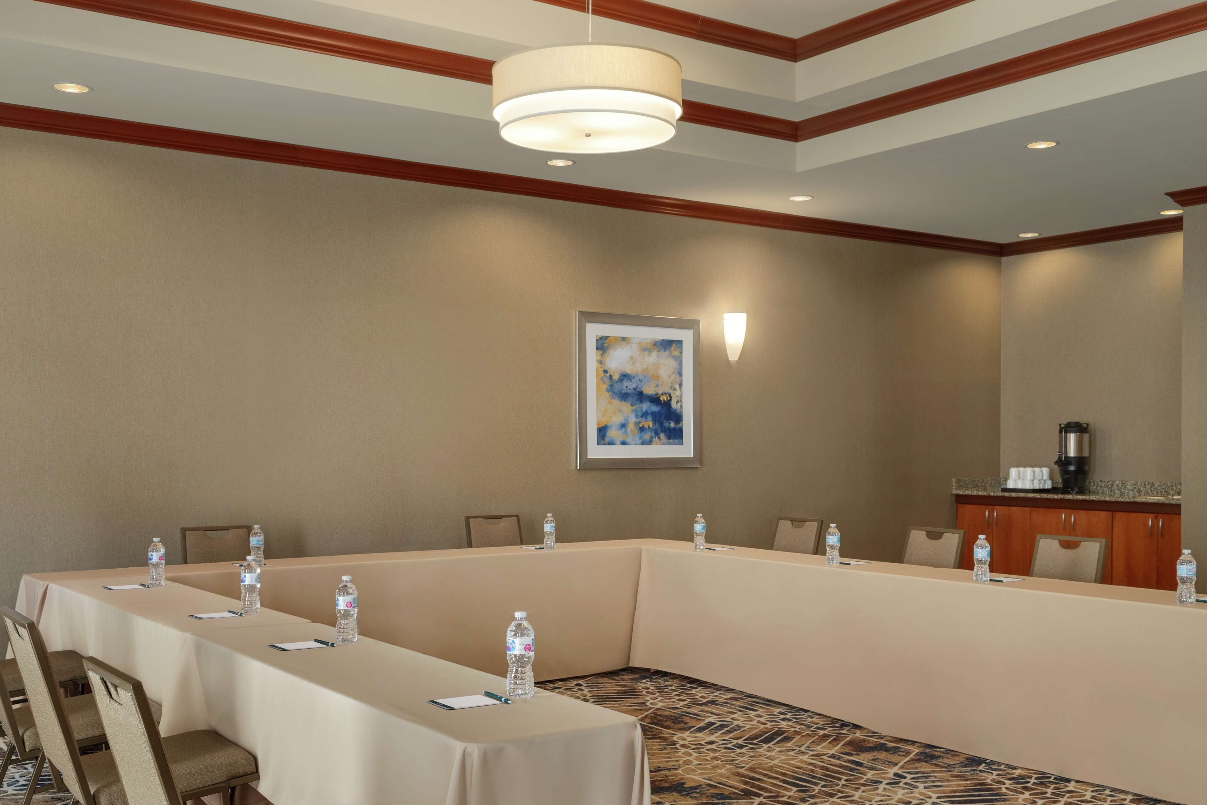 A conference room with a long table, chairs, water bottles, a painting, and a coffee machine.