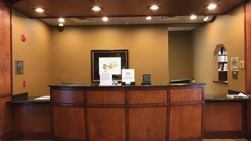 A reception desk with a framed picture above it, a bulletin board with a sign, and a small window with bookshelves.