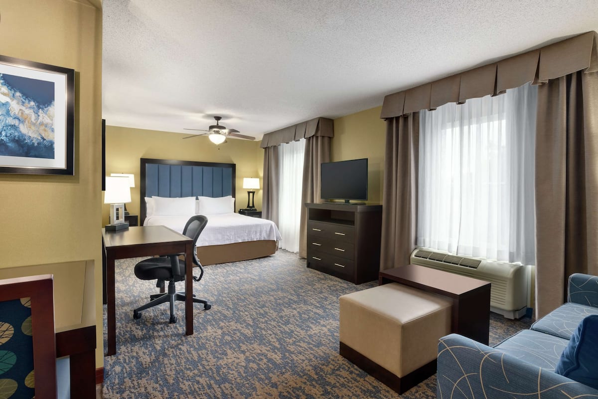 Ein Hotelzimmer mit Bett, Schreibtisch, Sessel, Fernseher und einer Couch.