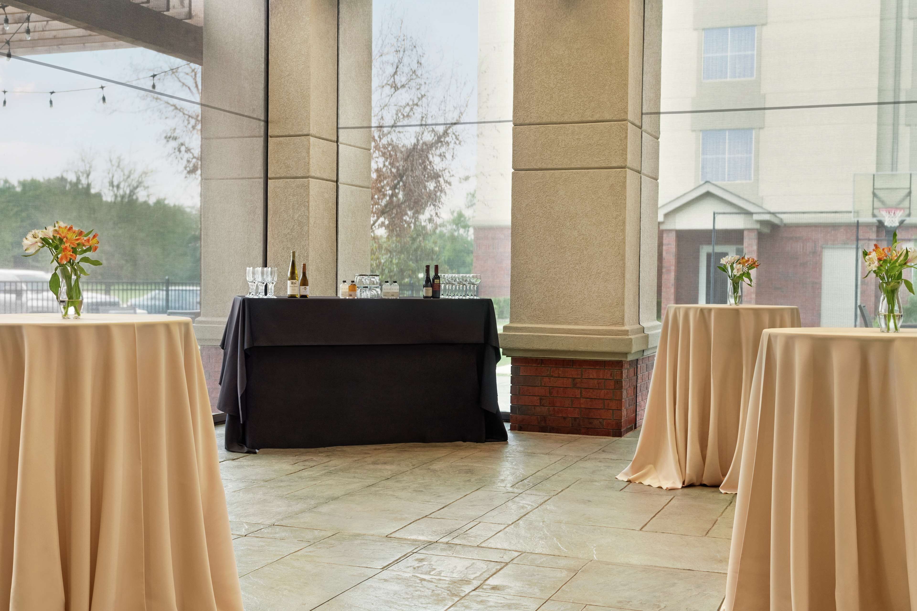 An indoor venue with tables set for an event, featuring a brick fireplace and large windows.