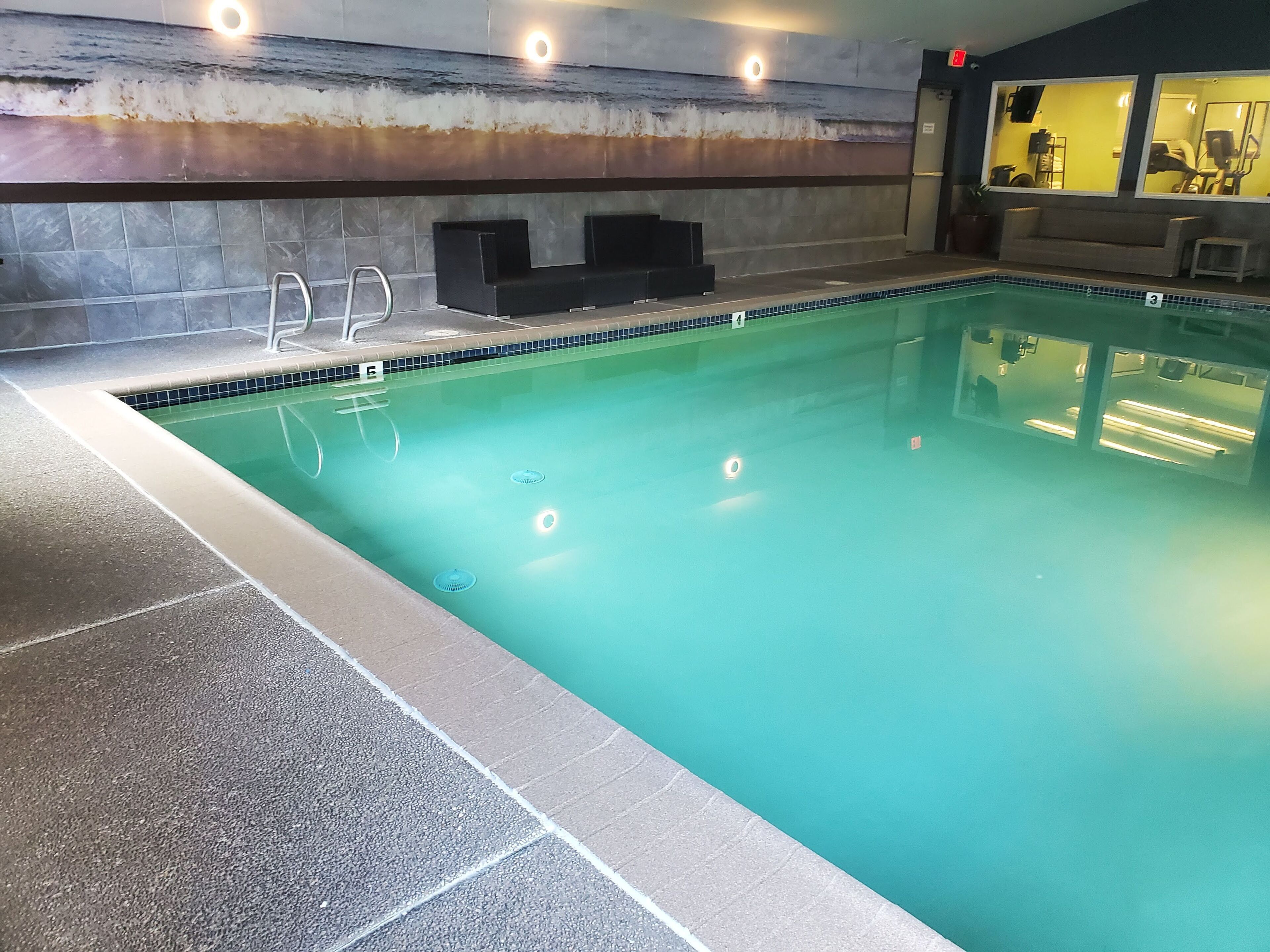 A swimming pool with a tiled edge, a metal ladder, and a wall with a textured design.