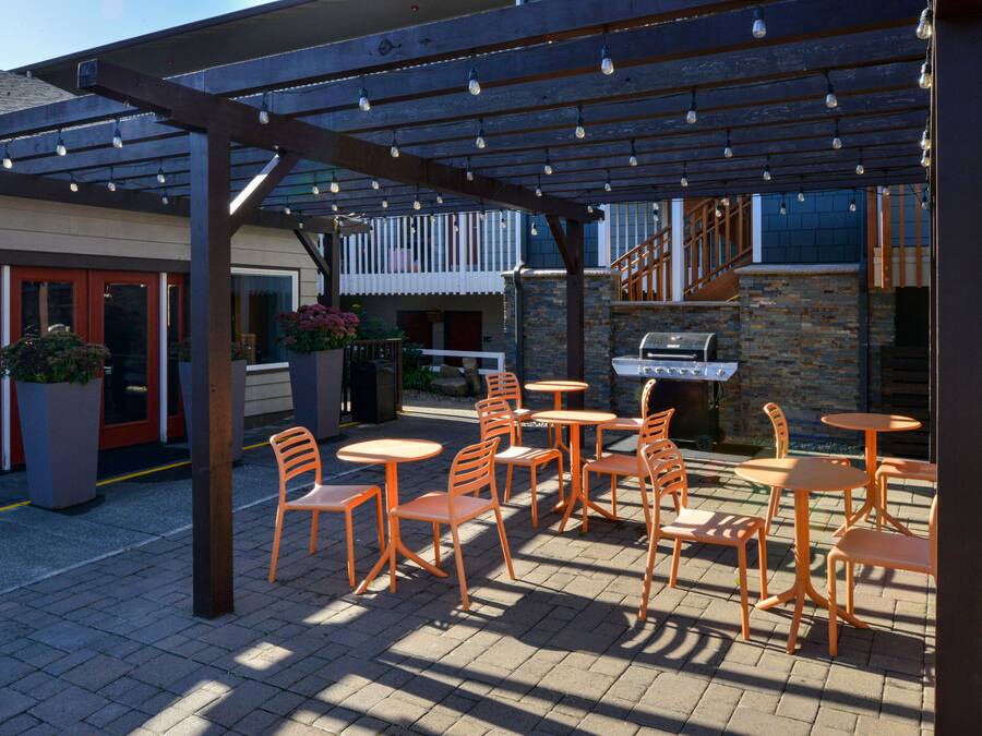 An outdoor patio with orange chairs and tables, a barbecue grill, and a covered area with string lights.