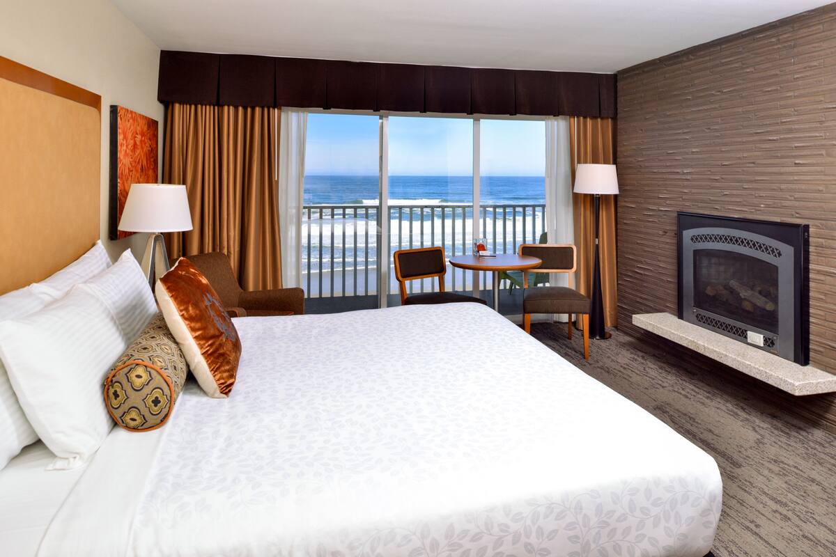 A hotel room with a large bed, a desk, a chair, a TV, and a view of the ocean.