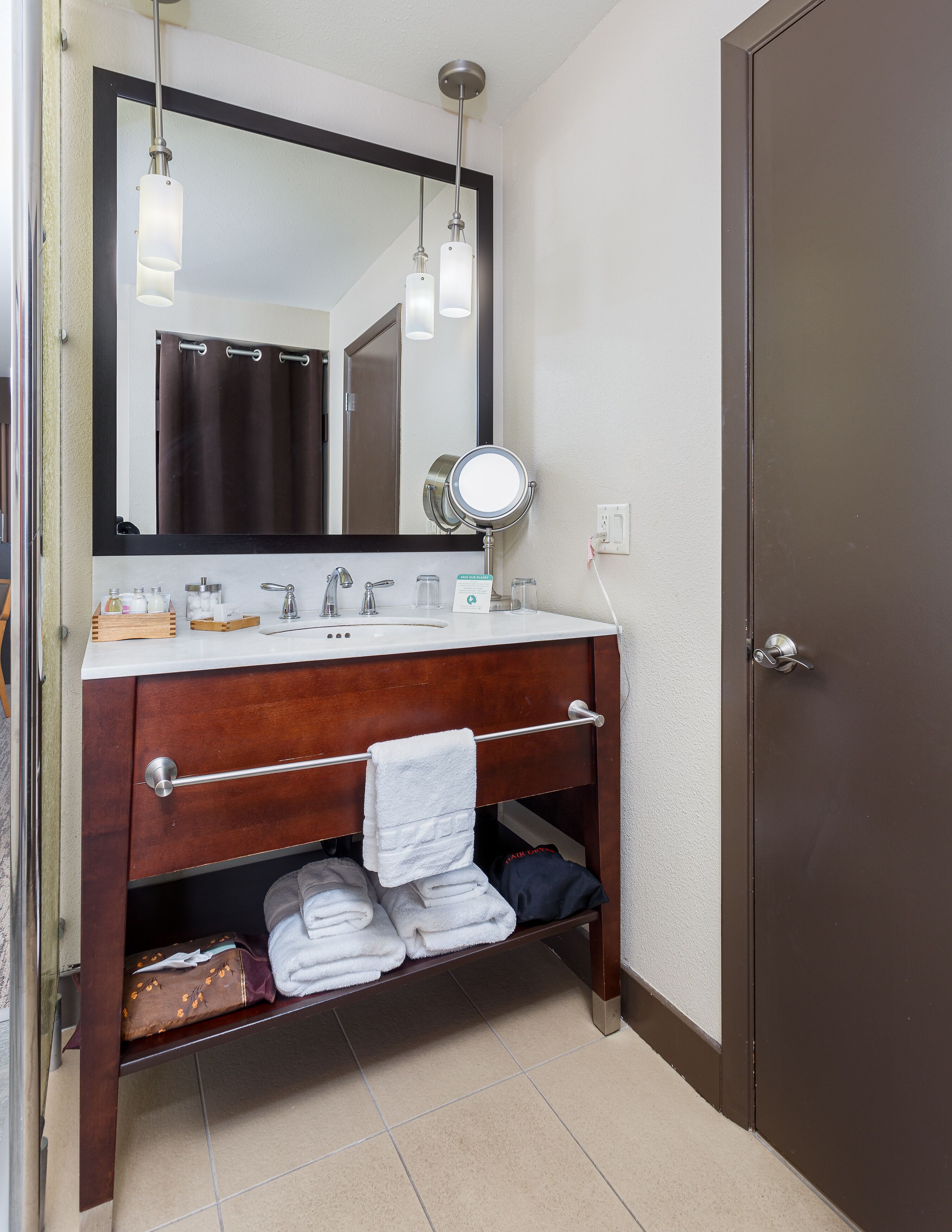A bathroom with a wooden vanity, a mirror, a towel rack, and a door.