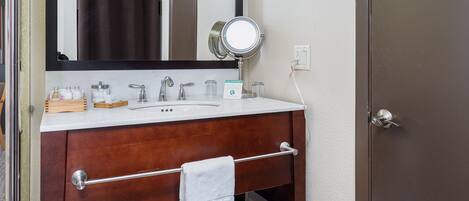 A bathroom with a wooden vanity, a mirror, a towel rack, and a door.