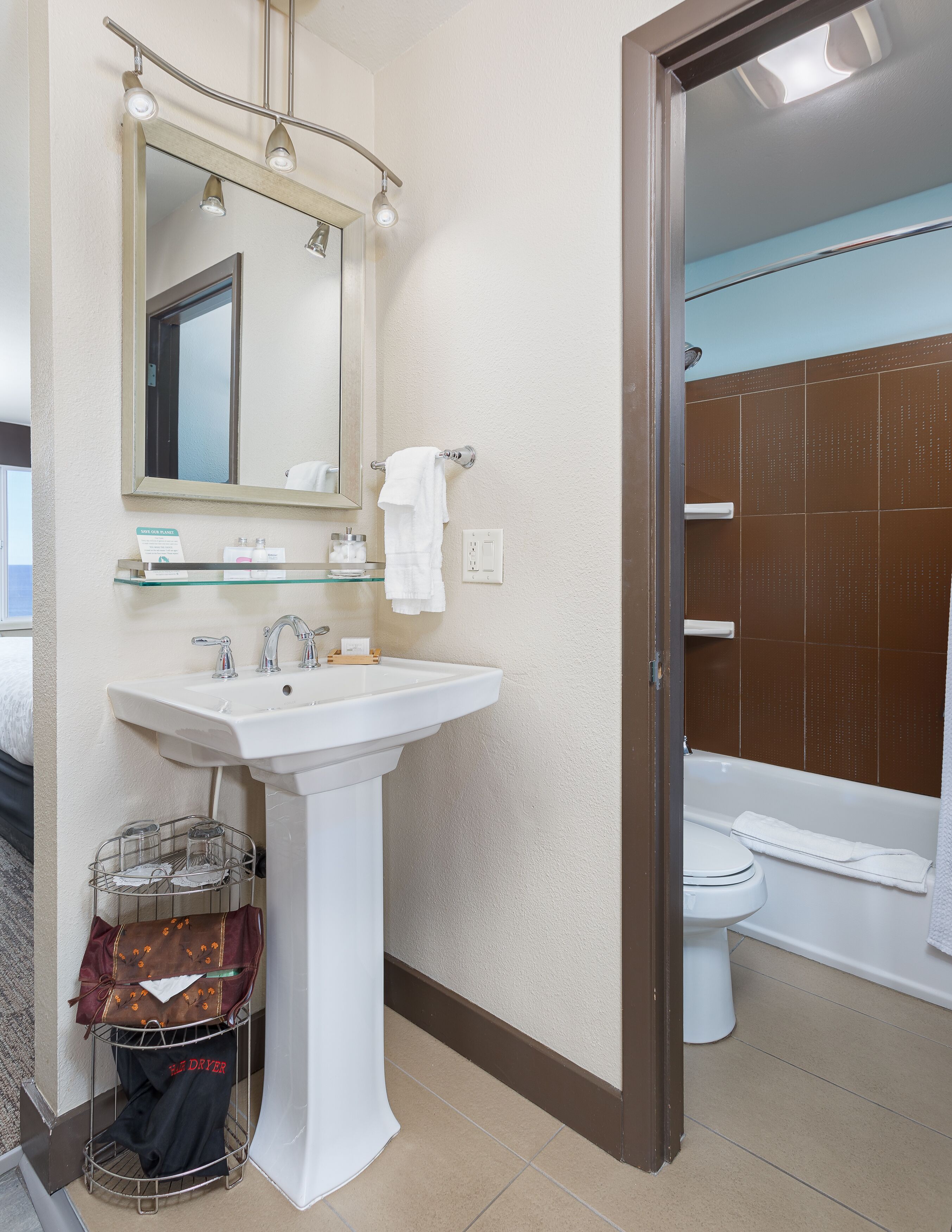 A bathroom with a white sink, mirror, and towel rack. There is a glass shelf above the sink and a shower curtain visible in the background.