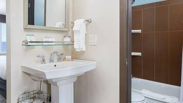 A bathroom with a white sink, mirror, and towel rack. There is a glass shelf above the sink and a shower curtain visible in the background.