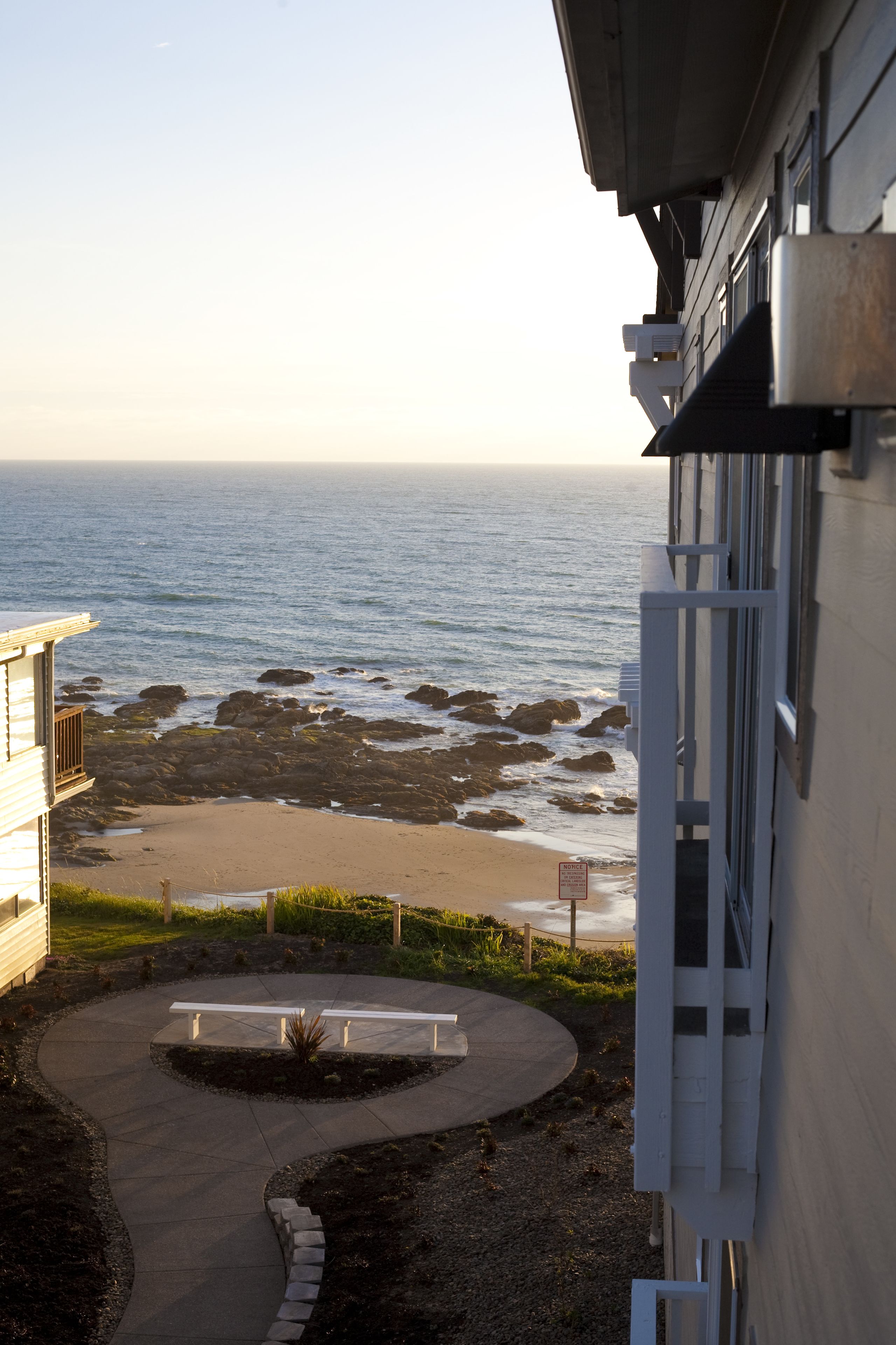 Vista d'una platja rocosa amb un camí corbat que condueix a una zona de seients, amb vista a l'oceà.