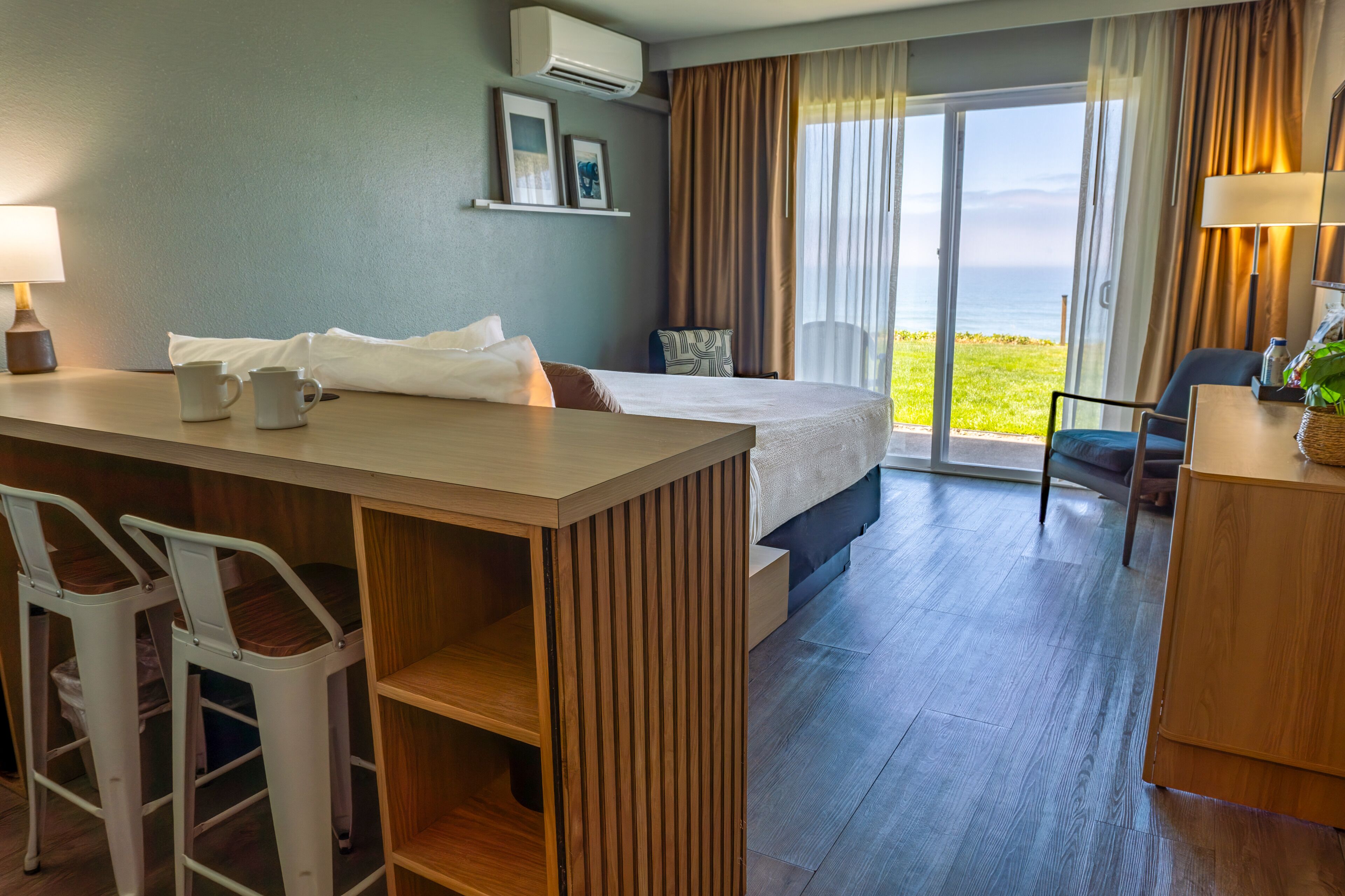 Ein Hotelzimmer mit Bett, Schreibtisch mit zwei Stühlen, Meerblick und einem Balkon.