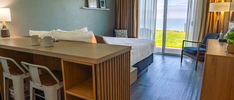 Ein Hotelzimmer mit Bett, Schreibtisch mit zwei Stühlen, Meerblick und einem Balkon.