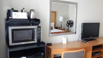 Quarto de hotel com cozinha compacta, incluindo micro-ondas, geladeira e máquina de café. Há uma TV, uma escrivaninha de madeira e uma cadeira.