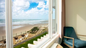 A room with a large window overlooking a beach, a blue chair, and a staircase leading to the beach. - The Coho Oceanfront Lodge (Lincoln City)