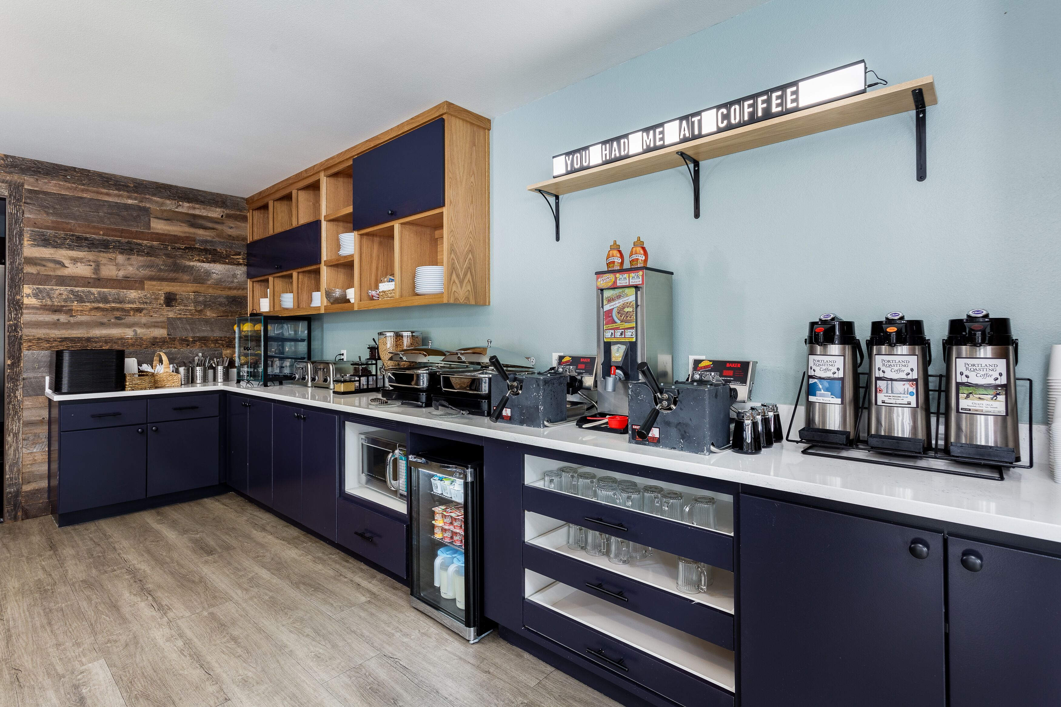 Una cocina moderna con estación de café, repisas de madera y un refrigerador expositor.