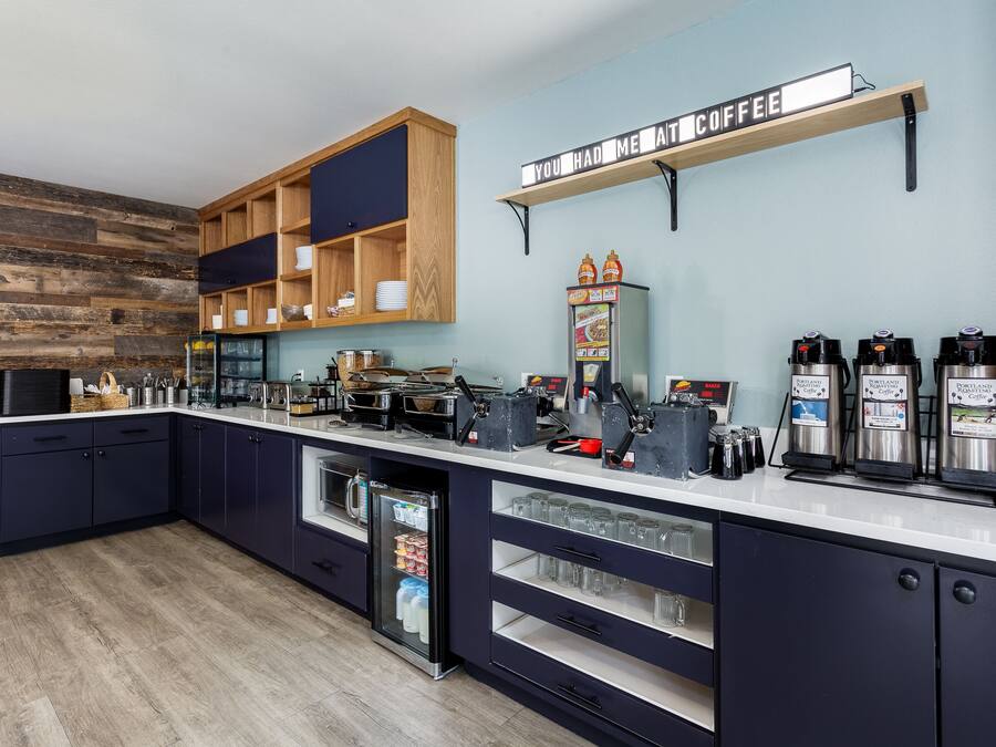 Una cocina moderna con estación de café, repisas de madera y un refrigerador expositor.