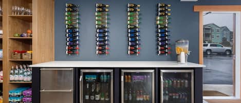 A bar area with a wall-mounted wine rack, a refrigerator with beverages, and a glass dispenser.