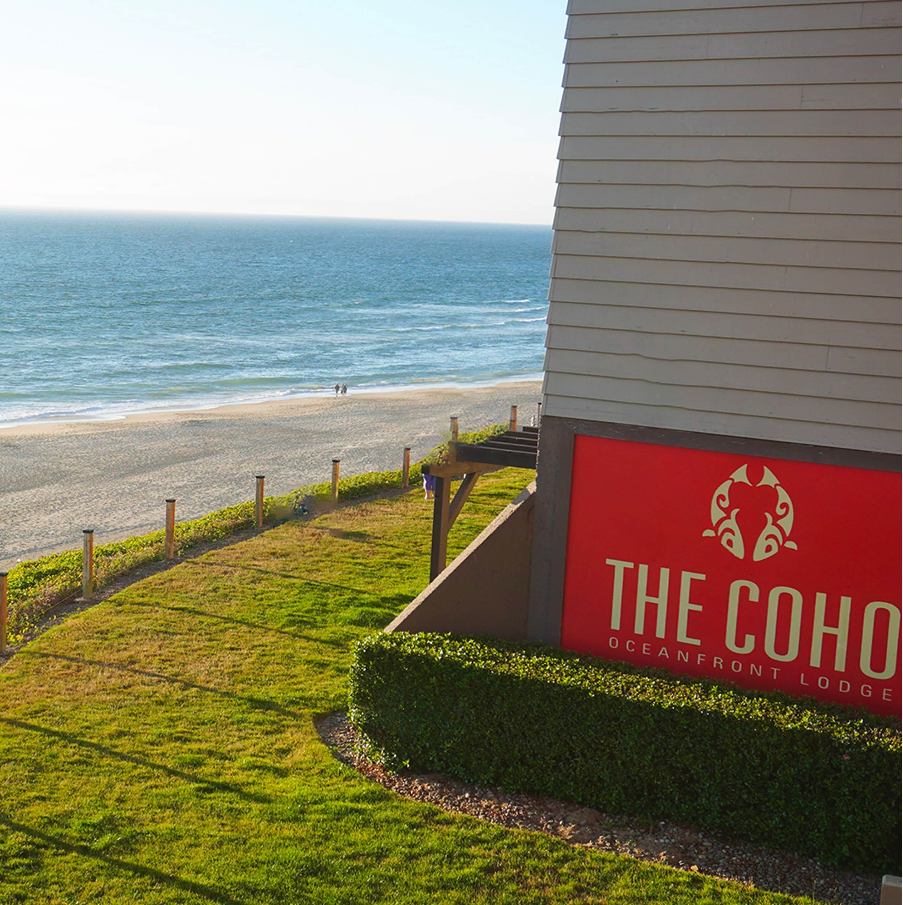 A coastal view with a sign for "The COHO Oceanfront Lodge" indicating a beachfront property.