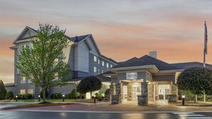 A hotel with a modern design, featuring a prominent entrance with a sign, a flagpole, and well-maintained landscaping. - Homewood Suites by Hilton Fayetteville (Fayetteville)