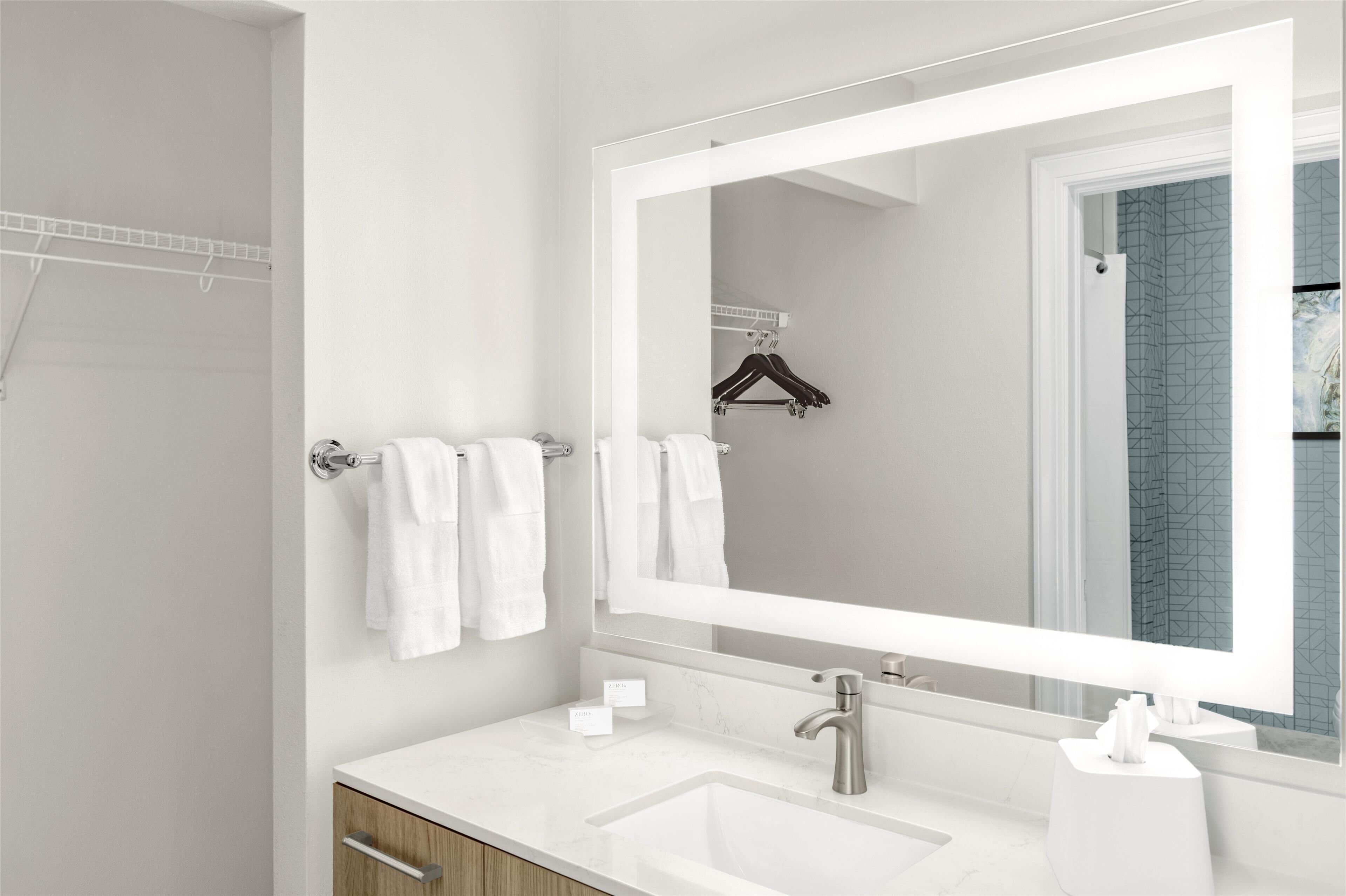 Un baño moderno con un espejo grande, lavamanos blanco y toallero.