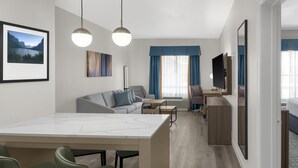 A modern hotel room with a dining area, a sofa, a TV, and a large window with curtains. - Homewood Suites by Hilton Fayetteville (Fayetteville)