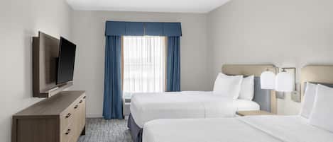 A hotel room with two beds, a TV on a wooden dresser, a ceiling fan, and a window with blue curtains.