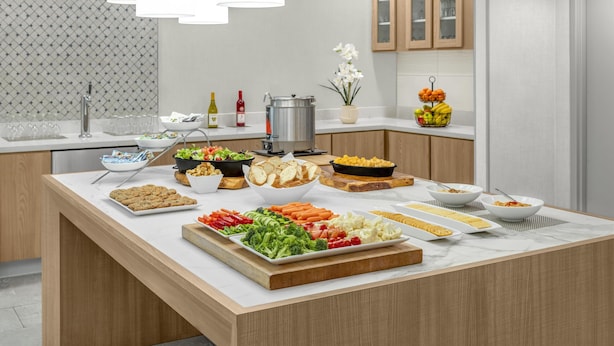 A modern kitchen with a marble countertop, various food items, and a decorative light fixture. - Homewood Suites by Hilton Fayetteville (Fayetteville)