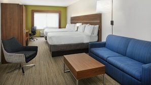 A hotel room with two beds, a blue sofa, a wooden coffee table, a checkered chair, and a desk with a lamp. - Holiday Inn Express Pensacola West - Navy Base by IHG (Pensacola)