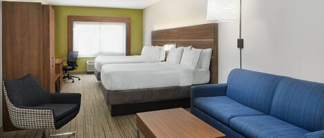 Une chambre d’hôtel avec deux lits, un canapé bleu, une table basse en bois, un fauteuil à carreaux et un bureau avec une lampe.