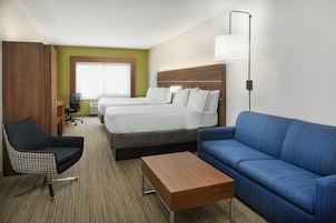 Une chambre d’hôtel avec deux lits, un canapé bleu, une table basse en bois, un fauteuil à carreaux et un bureau avec une lampe.