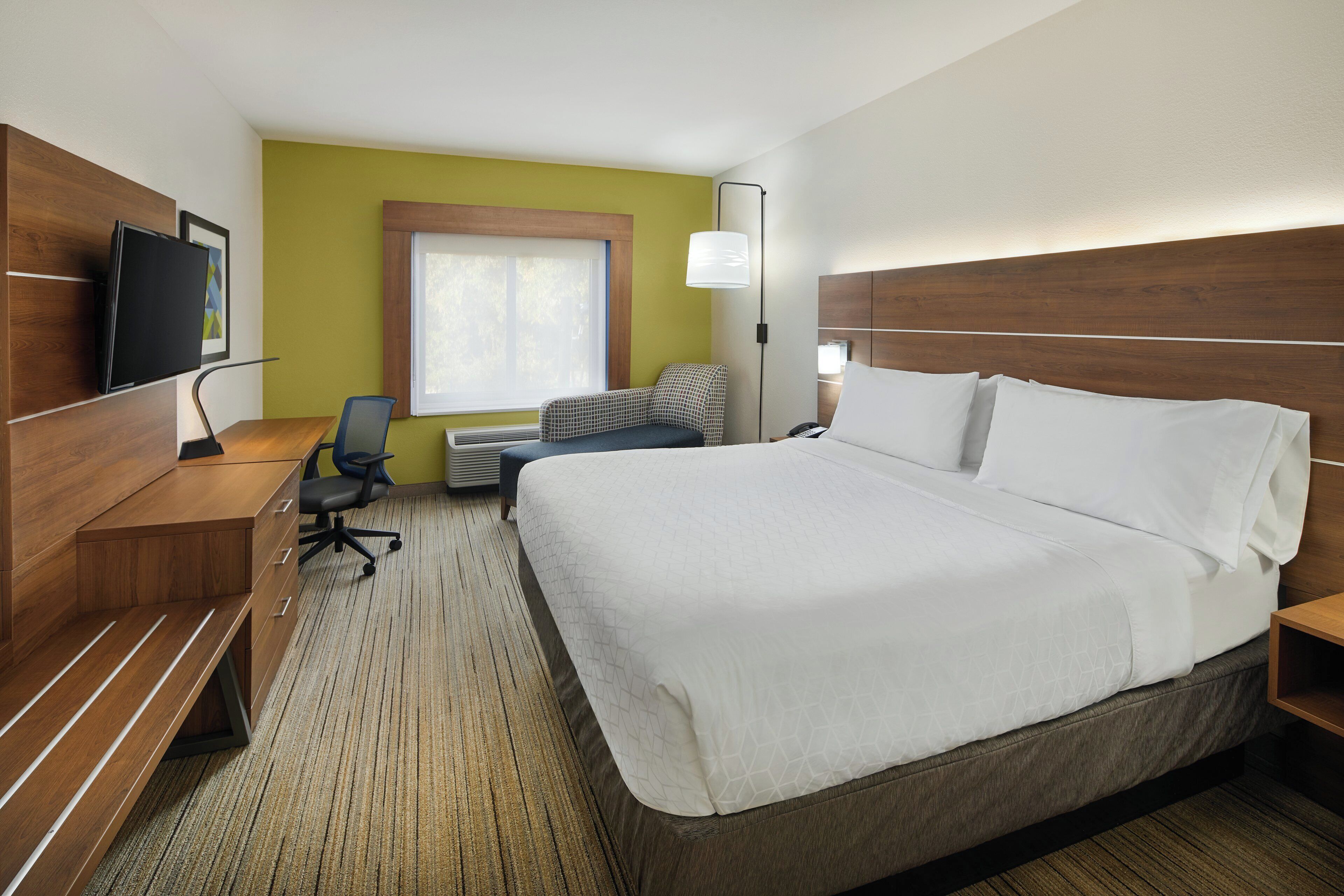 A hotel room with a bed, desk, chair, and a television.