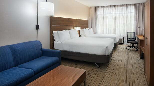 A hotel room with two beds, a blue sofa, a wooden table, and a desk with a chair. - Holiday Inn Express Pensacola West - Navy Base by IHG (Pensacola)