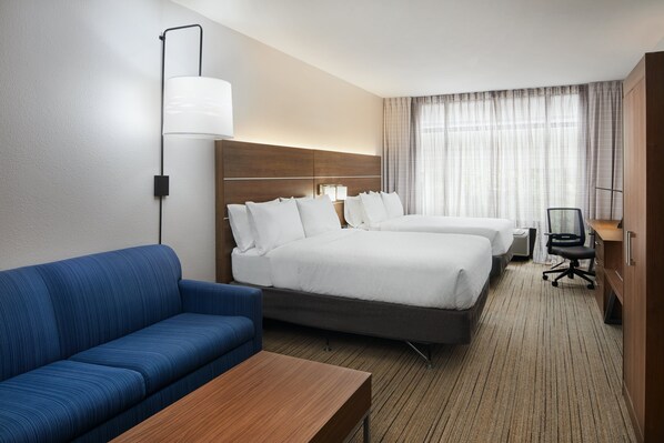 Habitación de hotel con dos camas, un sofá azul, una mesa de madera y un escritorio con una silla.