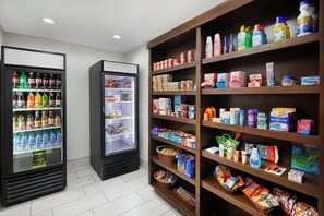 A self-service beverage area with multiple refrigerators stocked with drinks and a shelf with various food and household items. - Holiday Inn Express Pensacola West - Navy Base by IHG (Pensacola)