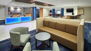 Un vestíbulo de hotel con mostrador de recepción, zona de estar y televisor.
