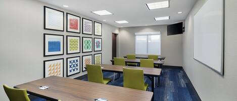 A conference room with a long table, several chairs, a projector screen, and framed artwork on the wall.