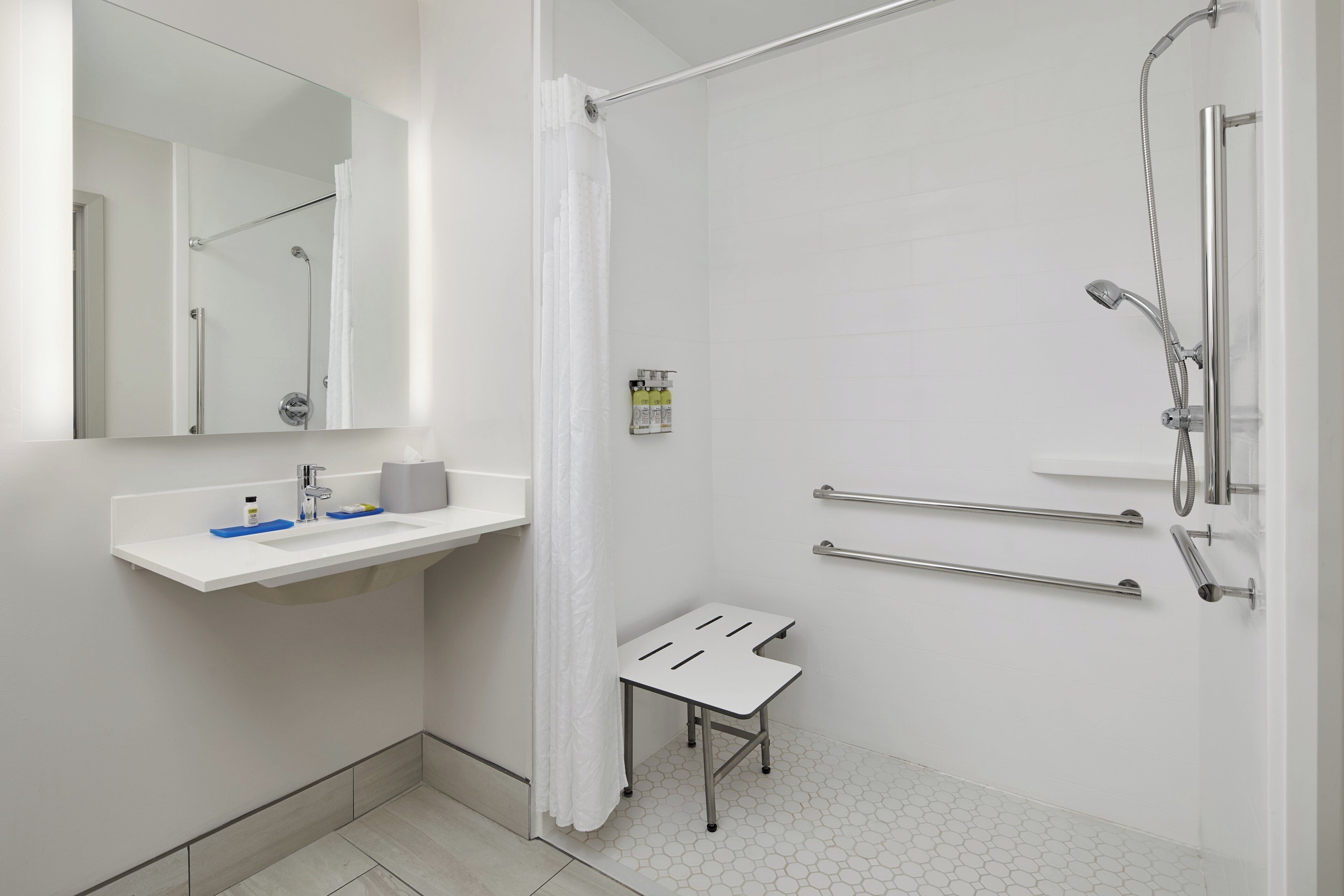 A modern bathroom with a shower, a sink with a mirror, and a small stool.