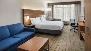 A hotel room with a bed, a blue sofa, a wooden desk, a chair, and a large window with curtains. - Holiday Inn Express Pensacola West - Navy Base by IHG (Pensacola)