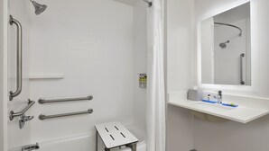 A modern bathroom with a walk-in shower, grab bars, a small step stool, and a sink with a mirror above it. - Holiday Inn Express Pensacola West - Navy Base by IHG (Pensacola)