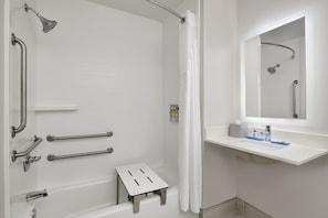 Un baño moderno con cabina de ducha, barras de apoyo, un taburete pequeño y un lavamanos con espejo.