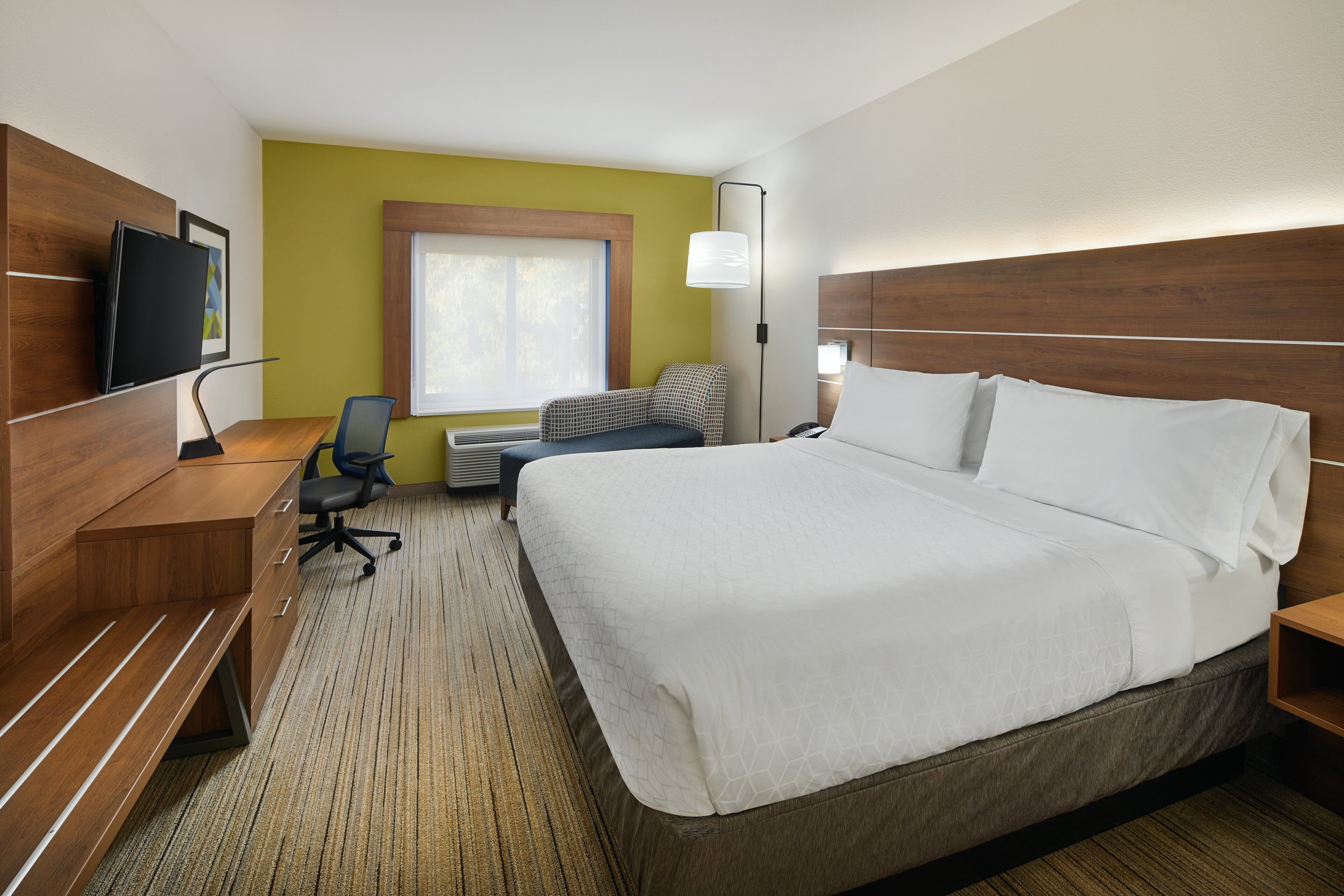 Habitación de hotel con una cama grande, un escritorio con silla, televisión y ventana con persianas.